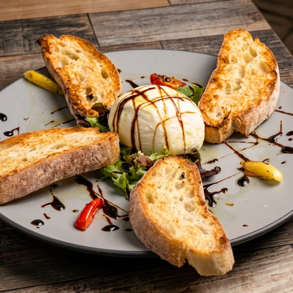 Burrata cheese with toasted bread, greens, and balsamic glaze on a grey plate.
