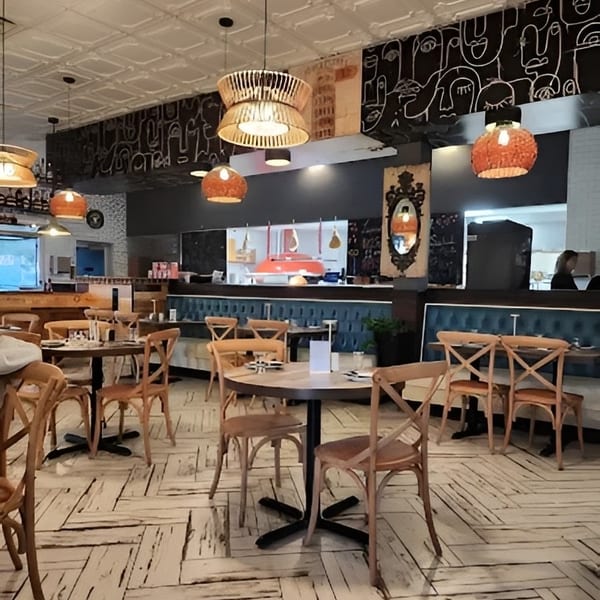 Cozy restaurant interior with wooden tables, chairs, unique lighting, and an open kitchen.