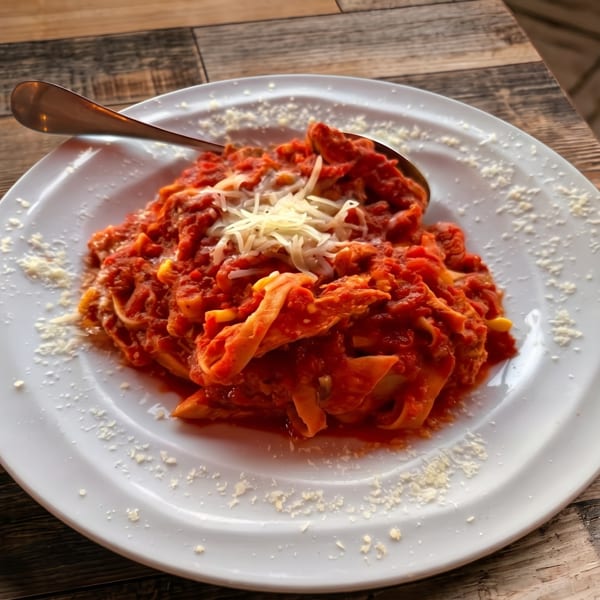 Plate of pasta with red sauce, shredded cheese, and a spoon on a wooden table.