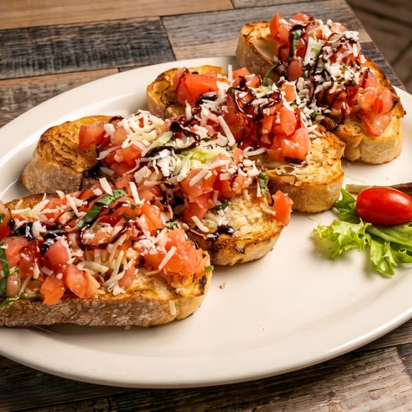Three bruschetta pieces with diced tomatoes, shredded cheese, basil, and balsamic glaze on a white plate.