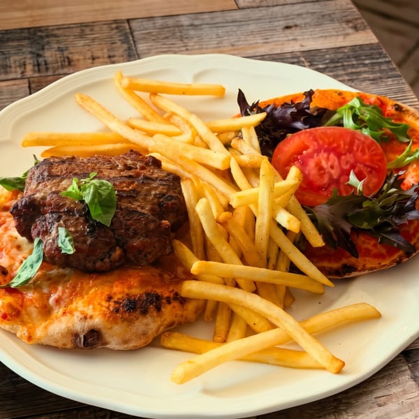 Grilled steak, golden fries, and two mini pizzas with tomato and greens on a white plate.